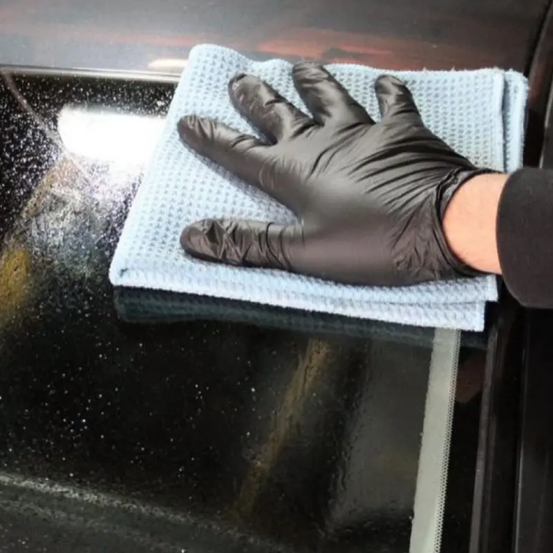 A person wearing a black glove wipes a car windshield clean