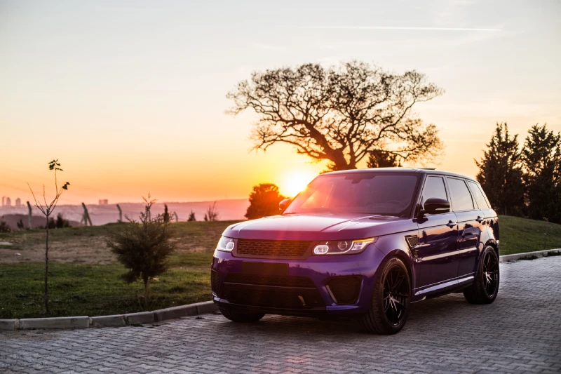 A blue coloured Range Rover SUV parked on the curb at sunset