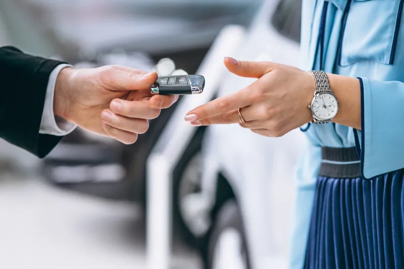 close shot of a female customer getting car keys handed over by a male sales executive at a car showroom