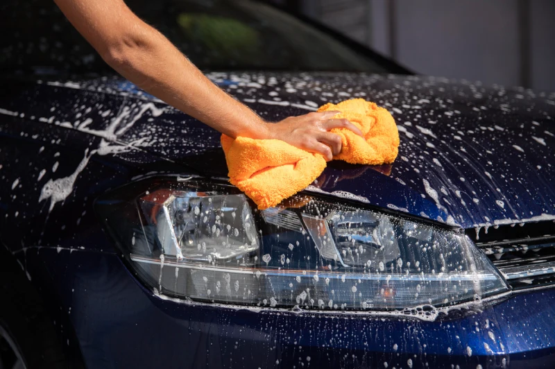 A blue car being washed with soap and cloth