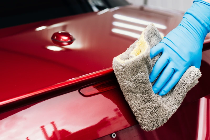 A red-coloured car being wiped dry with a microfiber cloth