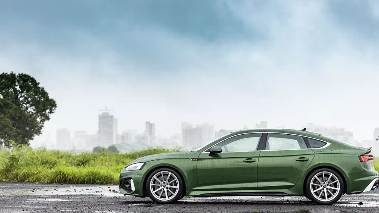 A green-coloured car parked on a rainy stretch with the cityscape in the background