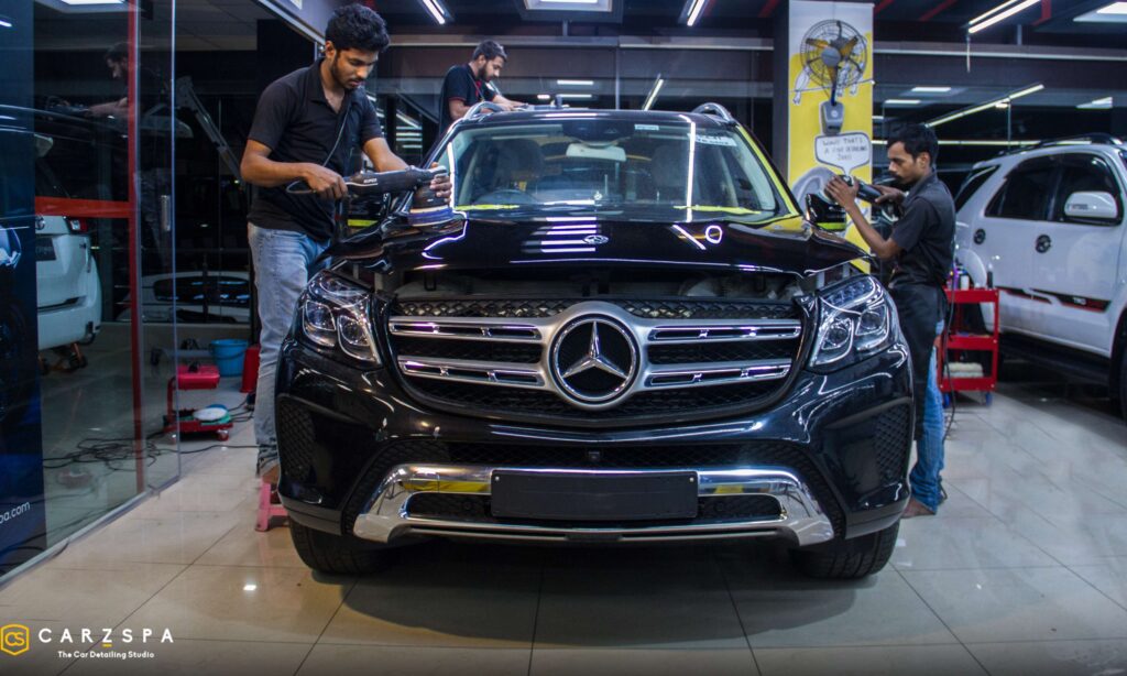 Two men working on detailing a black Mercedes SUV inside a detailing studio