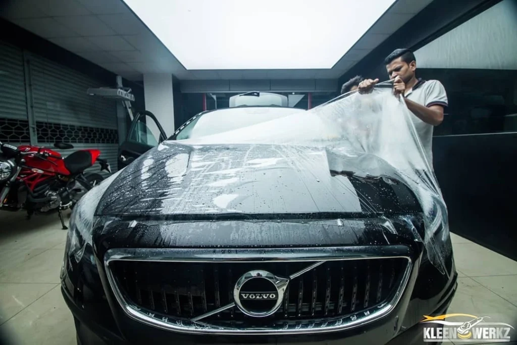 An Indian car detailer pulls a PPF from a panel of a black Volvo sedan