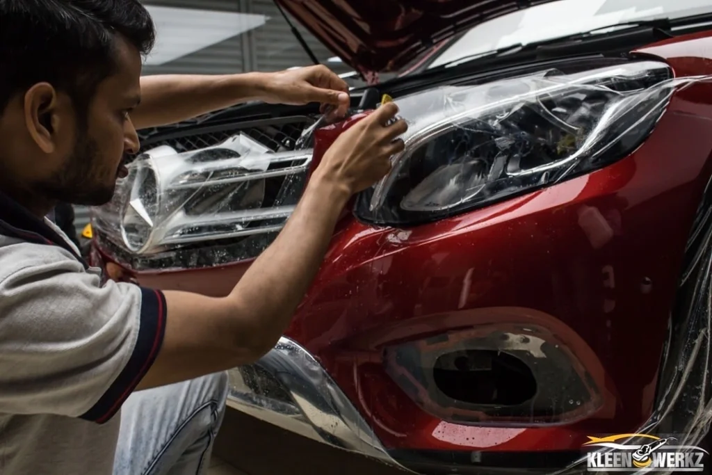 An Indian car detailer applies PPF on the front portion of a maroon sedan