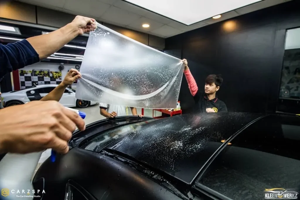 Workers apply clear film on a car’s bonnet