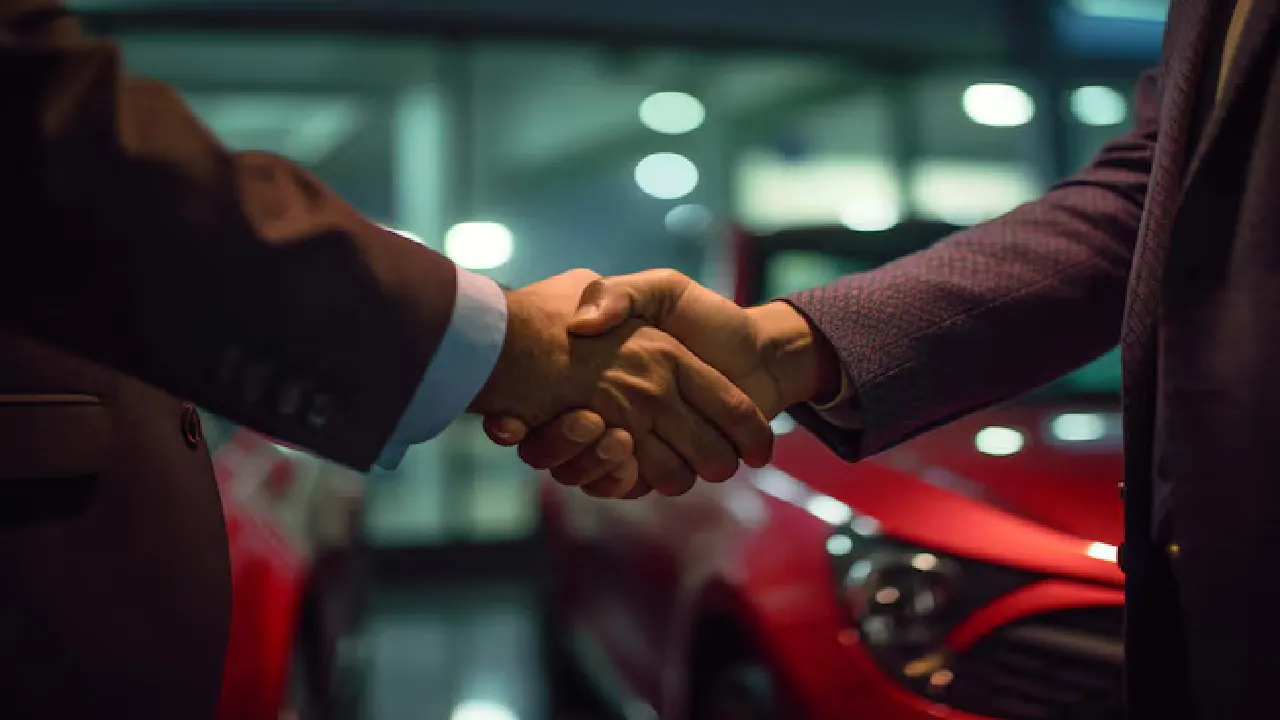 two hands shaking with cars parked in the background