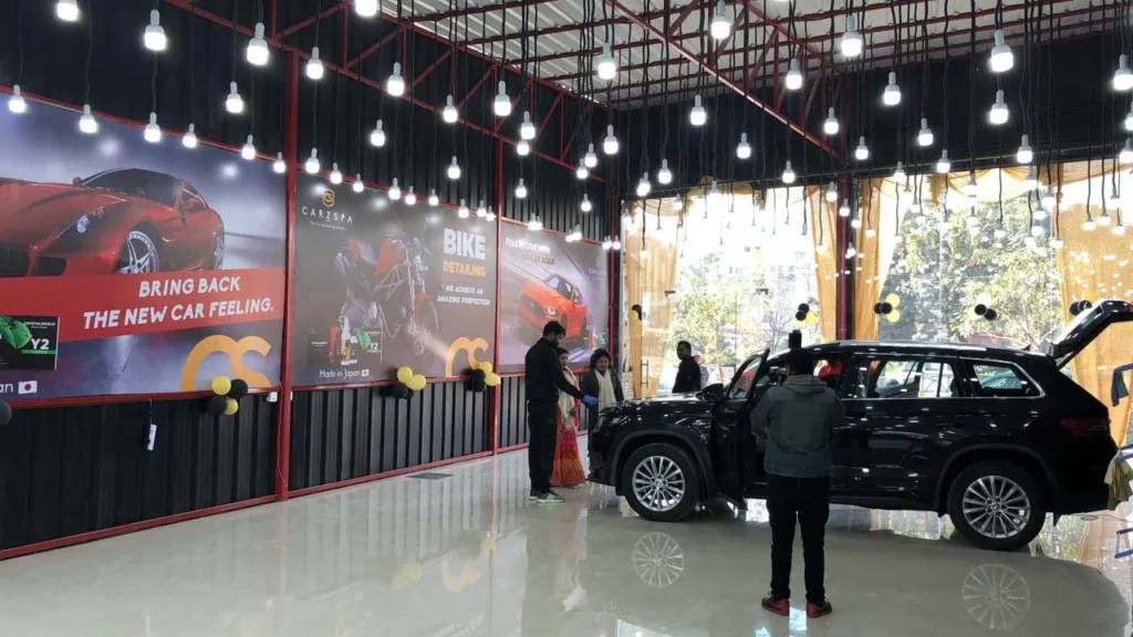 A black car parked inside a workshop while a worker inspects its engine