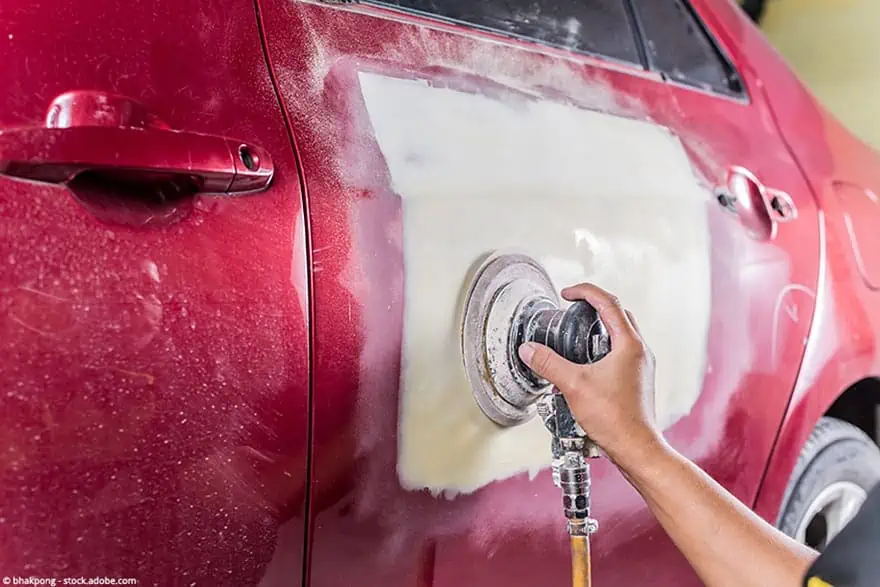 A worker removes paint from a car