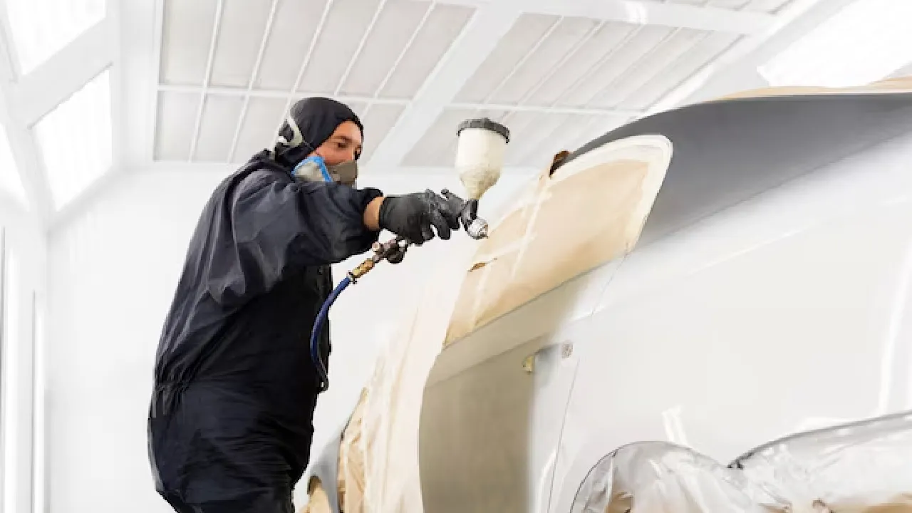 A worker in overalls paints a car with a spray painter gun