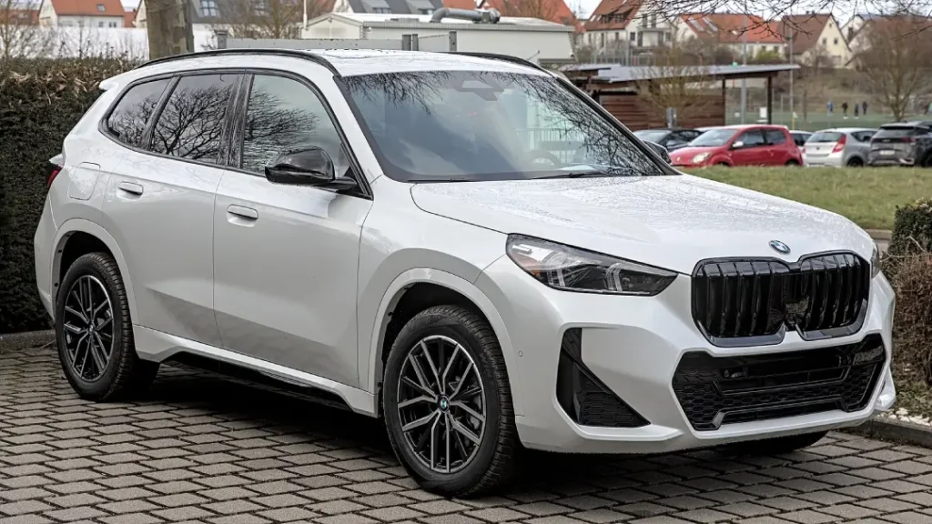 A white coloured BMW X1 parked outdoors in a residential area with some other cars visible in the background