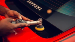 a worker runs a small polisher on the back panel of a red and black coloured Ferrari