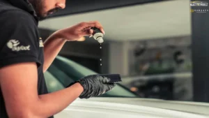 A worker drops ceramic coating on an applicator with a white-coloured car in the background inside a car detailing studio