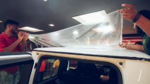 workers apply a paint protection film on the roof of a white SUV