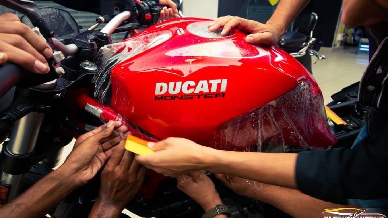 Workers install paint protection film on a red Ducati Monster bike