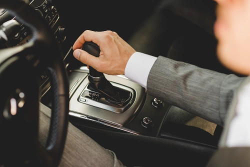 a man dressed in formals shifts the manual gear of his car while driving