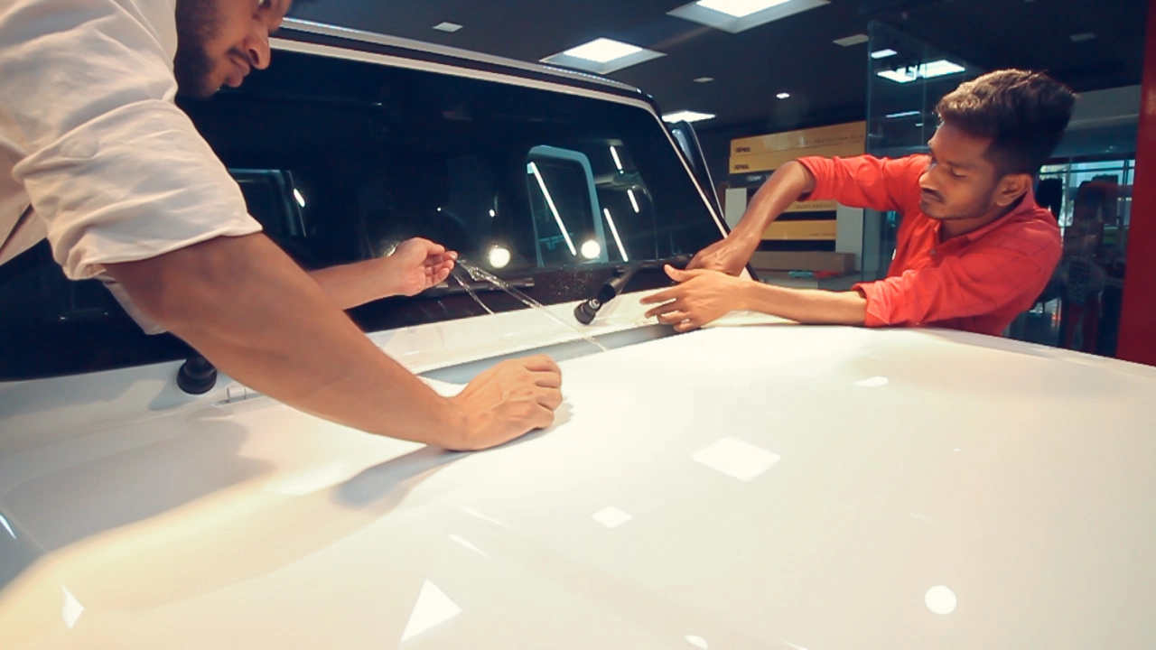 Two workers install a clear paint protection film on the hood of a white car