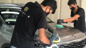 Workers polish a grey-coloured car inside a car detailing studio for paint protection