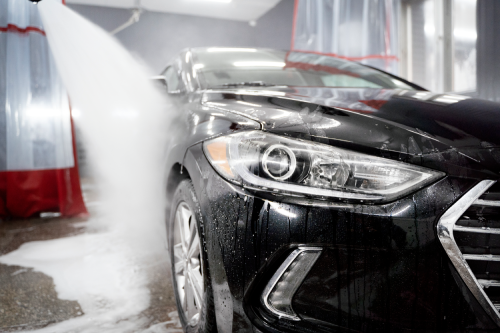 Water being sprayed on a black coloured sedan inside a workshop Water being sprayed on a black coloured sedan inside a workshop