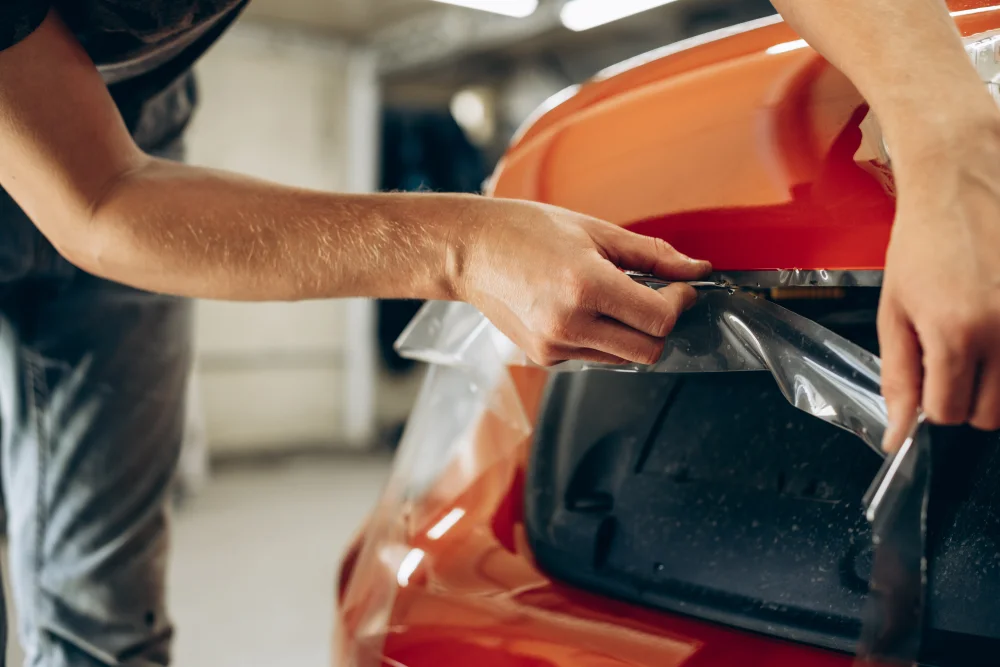 A worker applies a clear PPF on a red coloured car