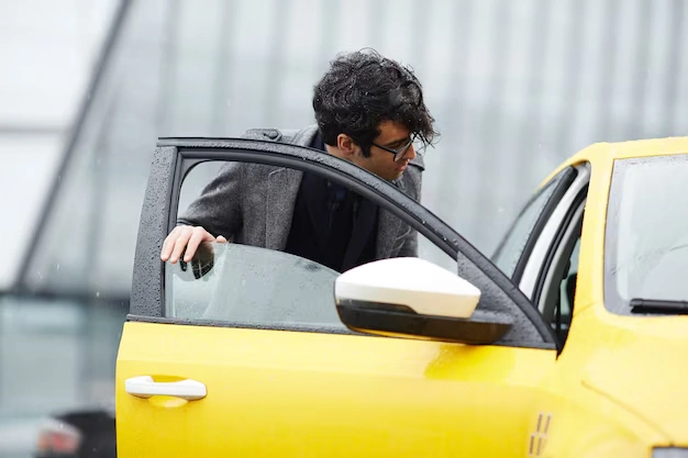 A young Indian man looks at his yellow car on the road while holding its door open