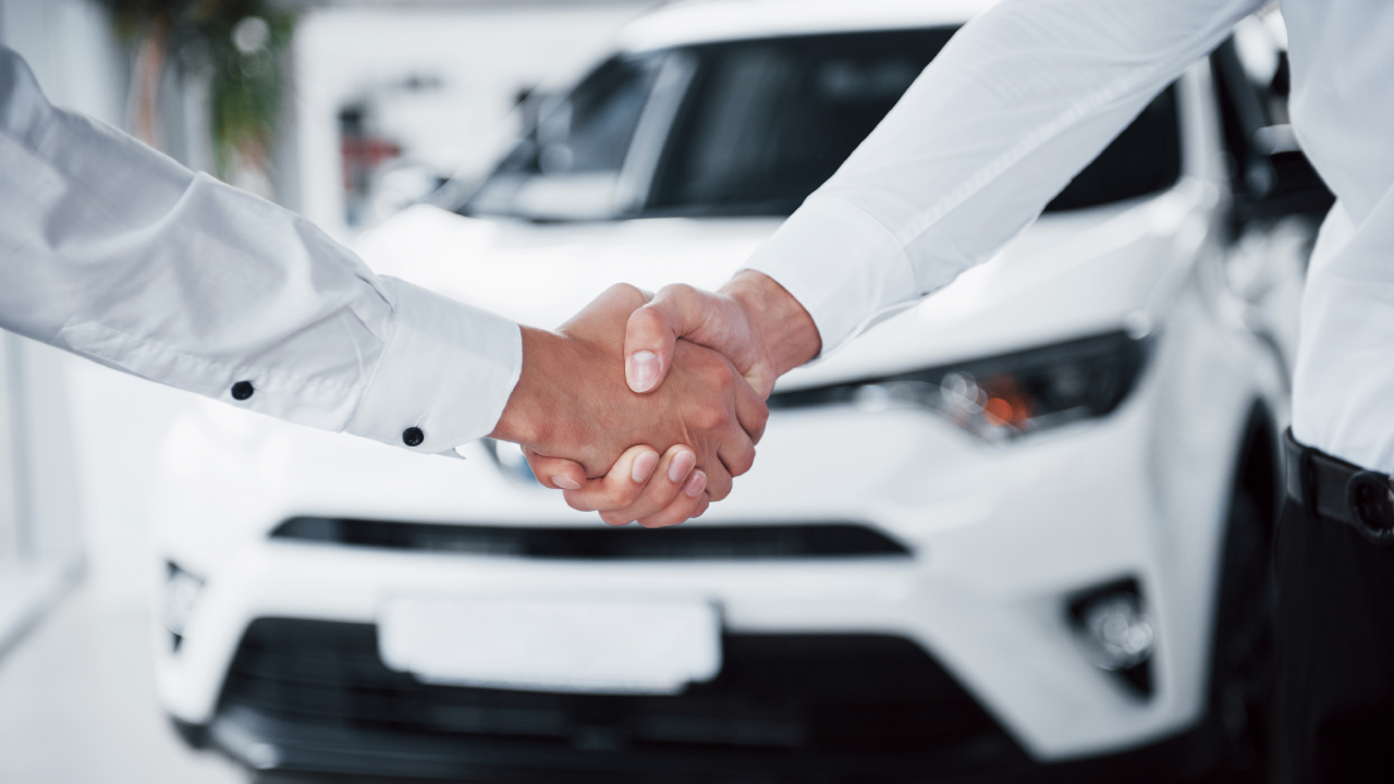 Close-up image of two hands shaking with a white car in the background