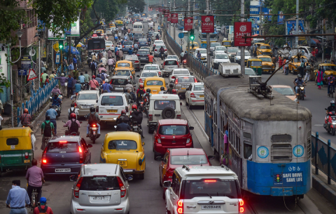 Image of a congested street in the evening in Kolkata with multiple cars, yellow taxicabs, two-wheelers and trams commuting on it