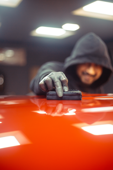 A worked wearing a hoodie applies ceramic coating to red coloured car’s surface